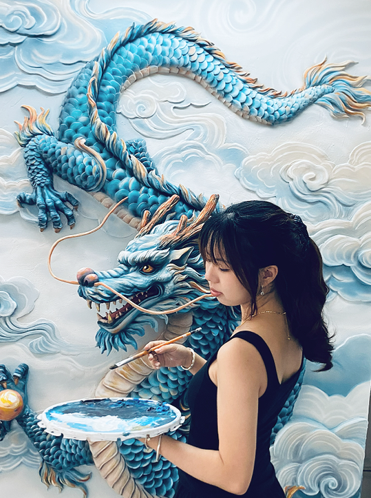 Person painting colour onto a blue dragon relief